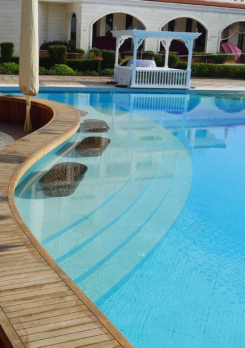 Premium blue glass mosaic tiles reflecting changing light across the luxury outdoor pool water