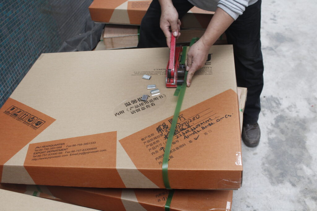 Custom Mosaic Tiles: From Design to Production 6 Worker tightening a packing strap around a carton at JNJMosaic