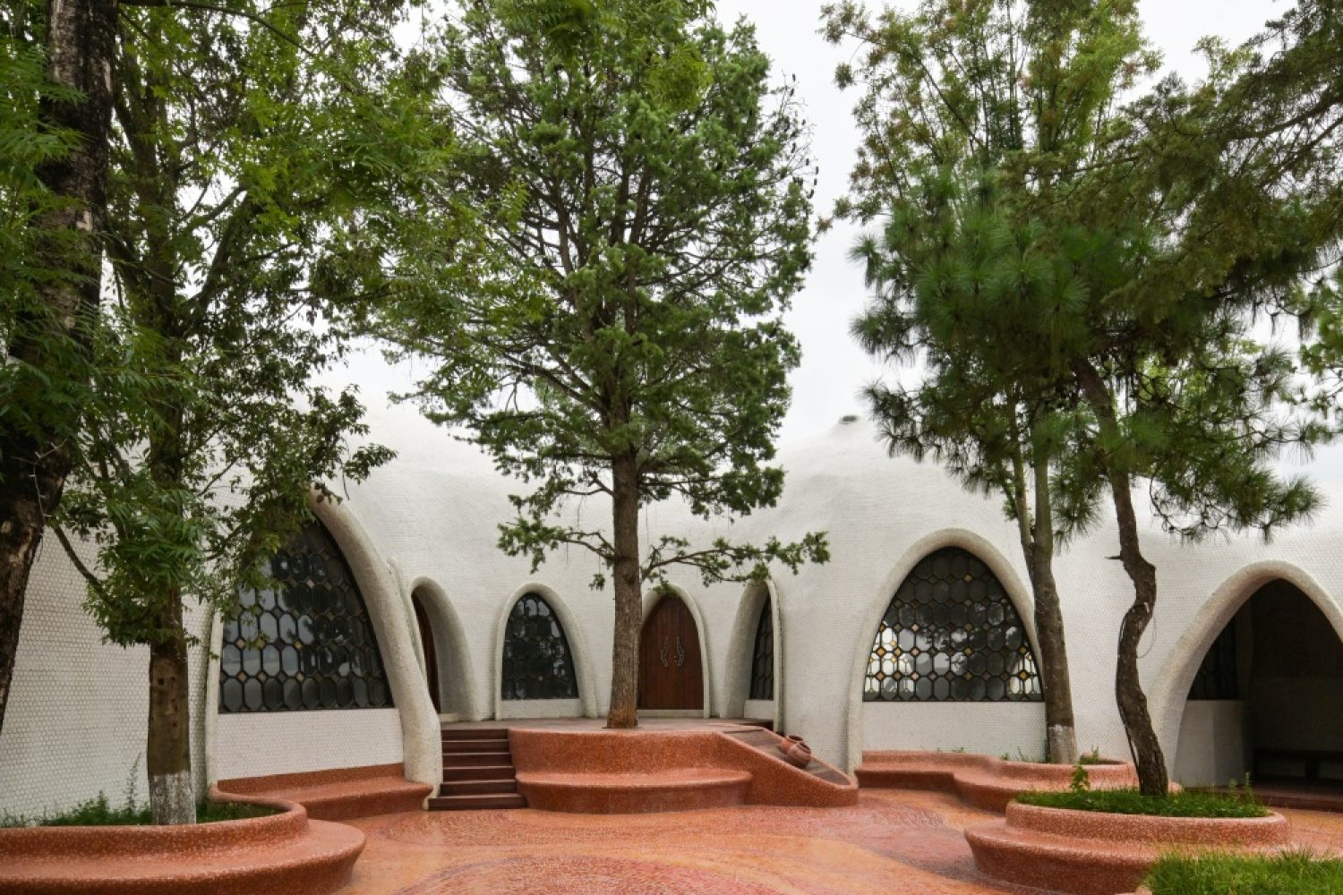 Red earth-inspired mosaic courtyard with integrated seating and trees at The Cloud Art Palace