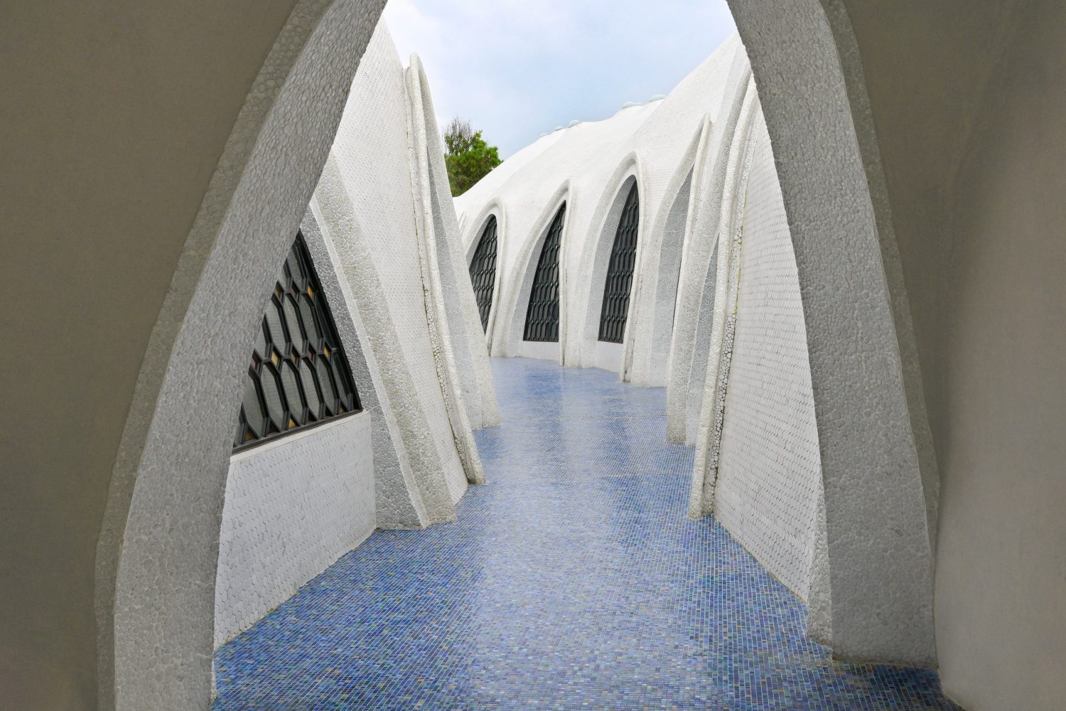 Blue glass mosaic corridor framed by arched white architecture
